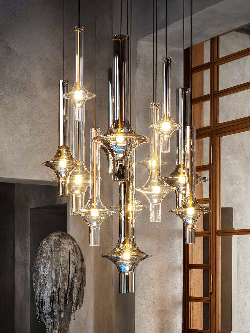 Lit Clérachic pendants cluster together in a stone-walled interior, beside a timber lattice door and a weathered stone sculpture.