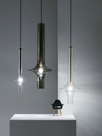 Three single Clérachic pendants in black, smoky and clear glass hang at staggered heights beside a plinth and a small chair figurine.