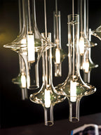 A tightly grouped cluster of lit Clérachic pendants is shown close, their glass heads catching warm light against a dark backdrop.