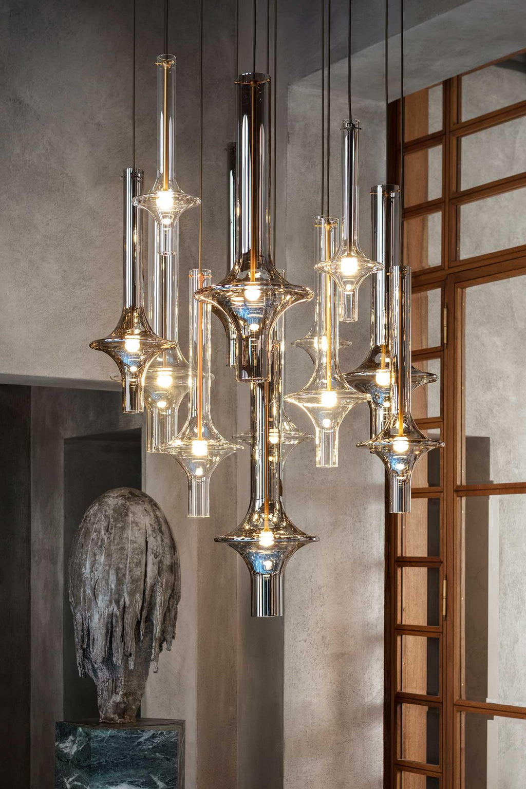 Clustered Clérachic pendants glow warmly in a stone-walled room, framed by a timber lattice door and a carved stone figure.