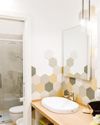 A single lit Clérachic pendant hangs in a bathroom lined with hexagon-patterned tiles, beside a mirror and a white basin.