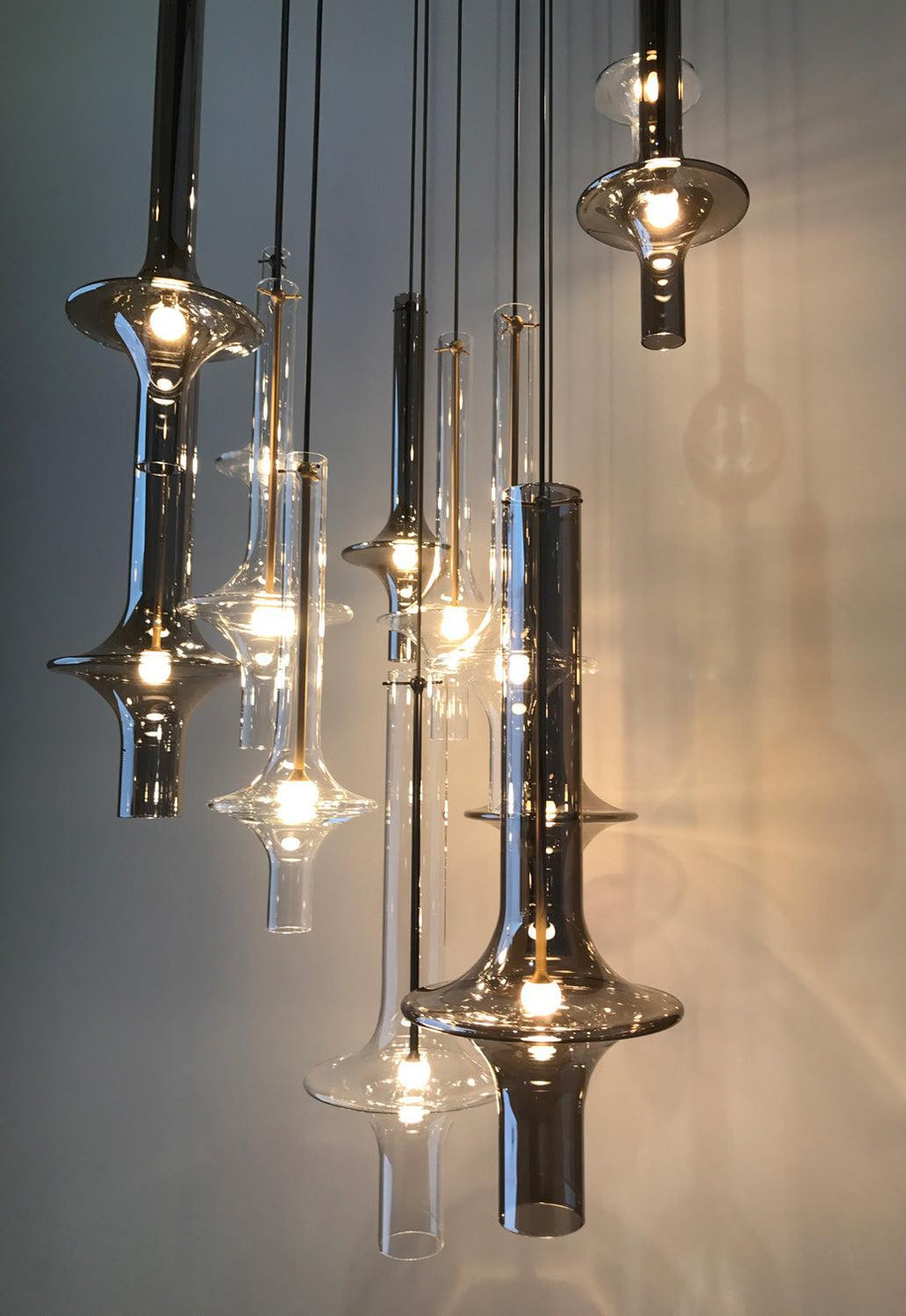 A close grouping of lit Clérachic pendants in clear and smoky glass catches the light against a dim ambient backdrop.