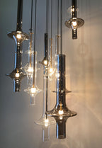 A close grouping of lit Clérachic pendants in clear and smoky glass catches the light against a dim ambient backdrop.