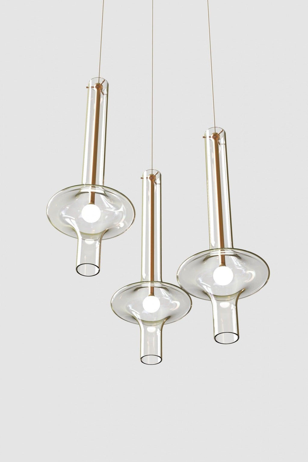 Three gold and clear-stemmed Clérachic pendants hang at different heights, unlit, against a light grey backdrop.