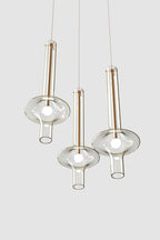 Three gold and clear-stemmed Clérachic pendants hang at different heights, unlit, against a light grey backdrop.