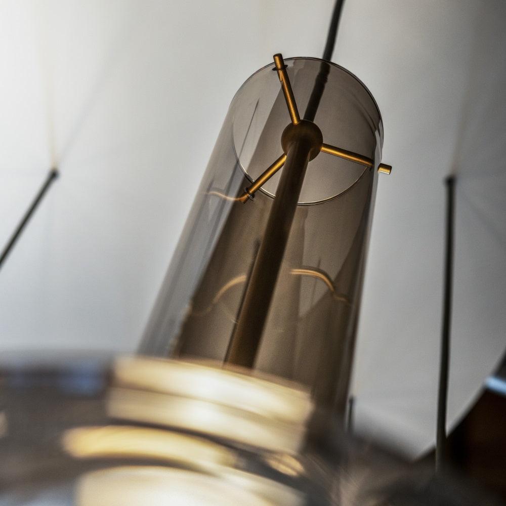 A close view inside a smoky glass shade shows the gold cross-bar bulb holder at the centre of this Clérachic pendant.