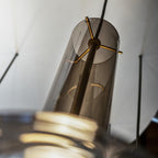 A close view inside a smoky glass shade shows the gold cross-bar bulb holder at the centre of this Clérachic pendant.