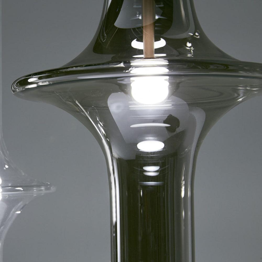 A close view of this Clérachic pendant's flared glass base shows the lit bulb through smoky grey glass.
