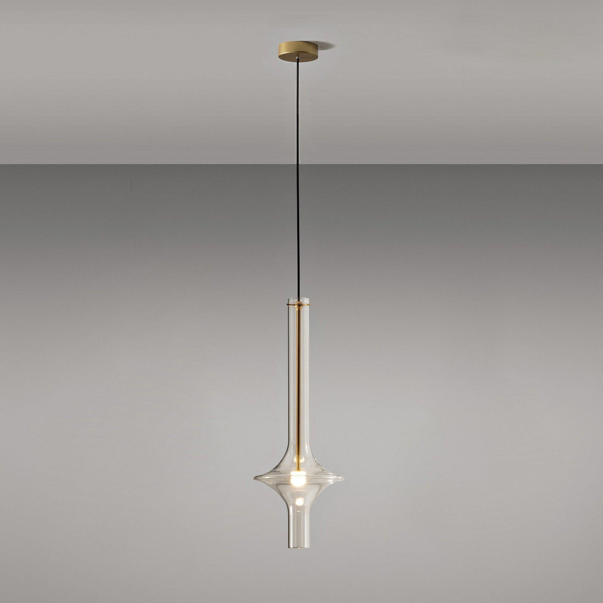 A single gold-stemmed Clérachic pendant with a matching gold ceiling canopy hangs against a plain grey backdrop.