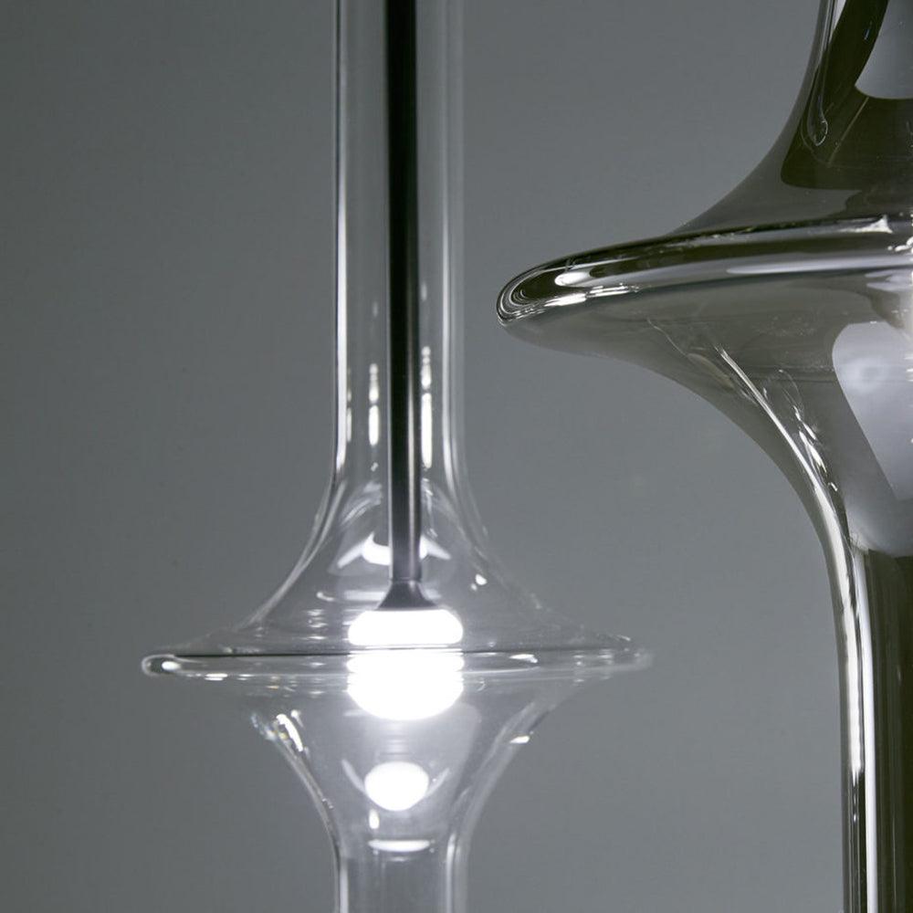 A macro view of this Clérachic pendant shows its neck narrowing into the flared clear glass base around a lit bulb.