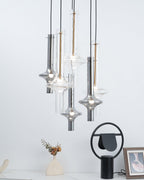 A cluster of gold, black and clear-stemmed Clérachic pendants hangs above a round side table with a vase and an orange strap chair.