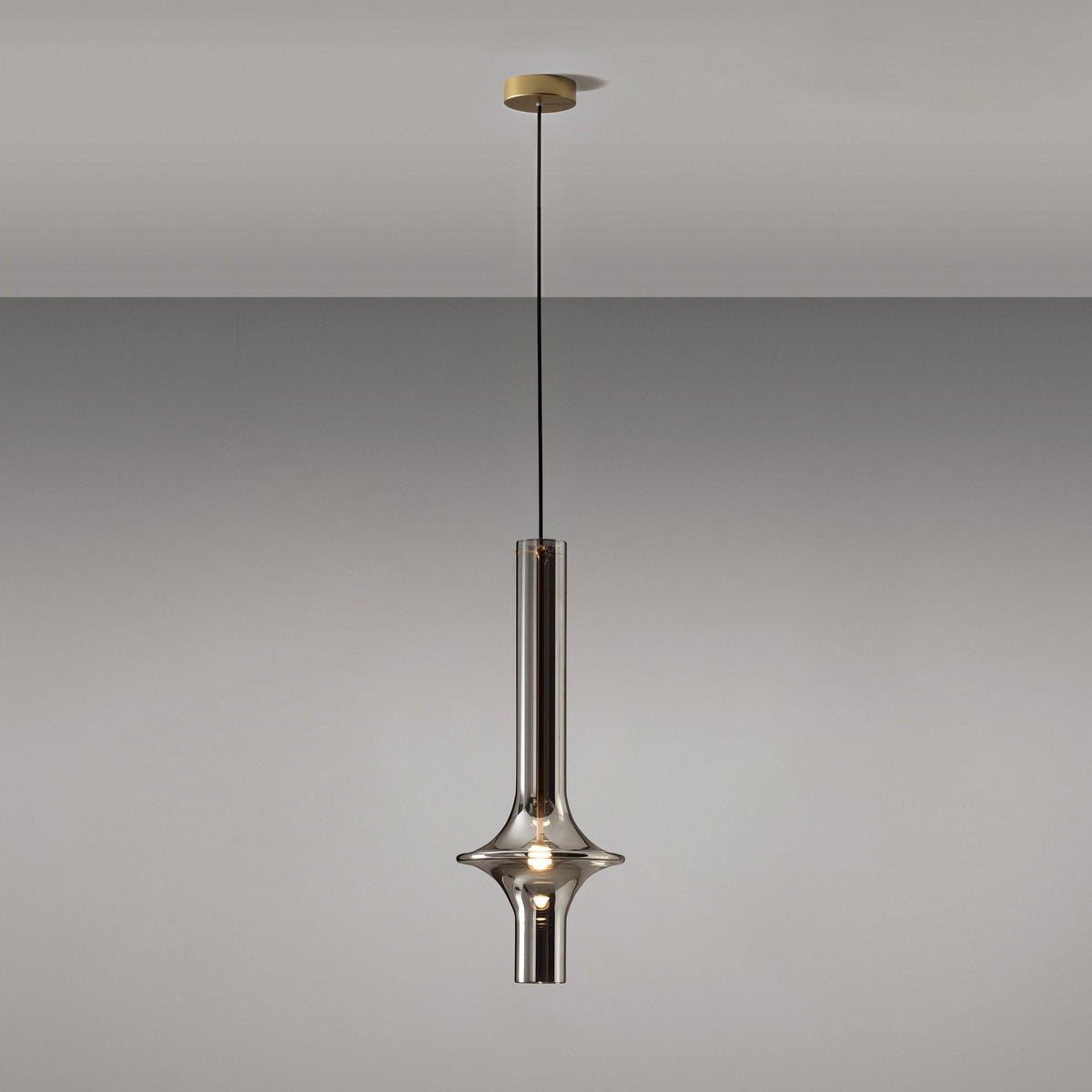 A single gold-stemmed Clérachic pendant in smoky grey glass hangs unlit against a plain grey backdrop, its gold canopy visible above.