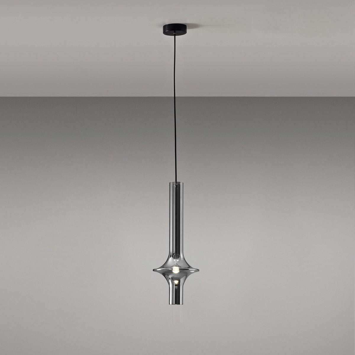 A single black-stemmed Clérachic pendant in smoky grey glass hangs unlit against a plain grey backdrop, its black canopy visible above.