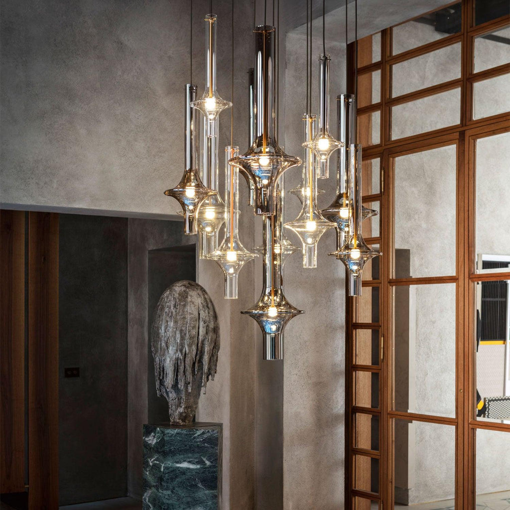 Gold and black-stemmed Clérachic pendants glow together in a stone-walled loft, beside a carved stone sculpture and a timber lattice door.