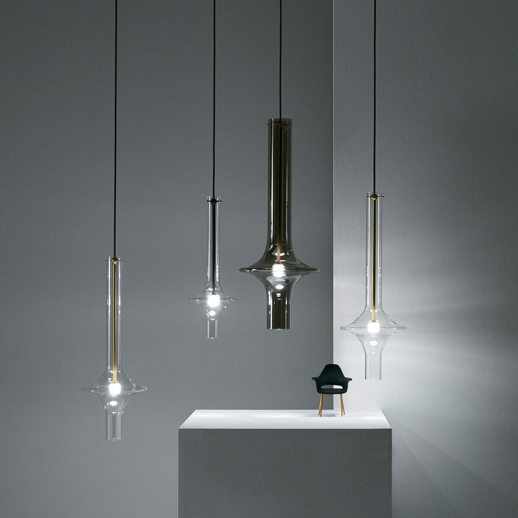 Four single Clérachic pendants in black, smoky and clear glass hang at staggered heights beside a small chair figurine on a plinth.