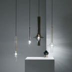 Four single Clérachic pendants in black, smoky and clear glass hang at staggered heights beside a small chair figurine on a plinth.