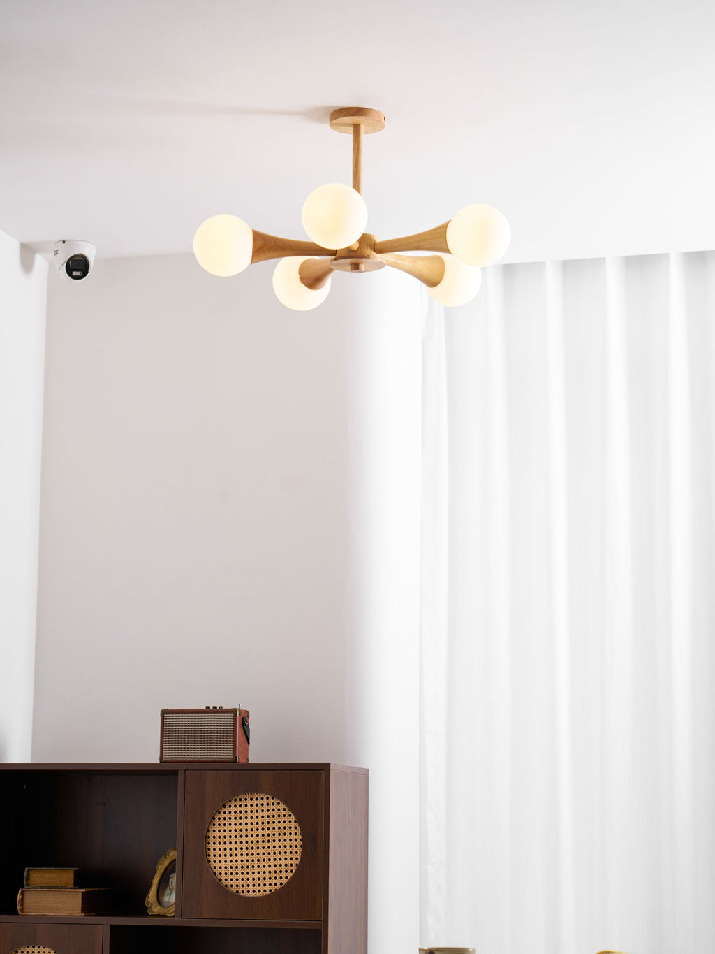 Mounted in a curtained corner with a small wall sensor visible nearby, this Clérachic chandelier glows above the dark wood cabinet.