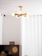 Mounted in a curtained corner with a small wall sensor visible nearby, this Clérachic chandelier glows above the dark wood cabinet.