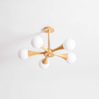 Side-angled view on a soft grey background, this Clérachic chandelier's ceiling mount sits to one side with its arms fanning right.
