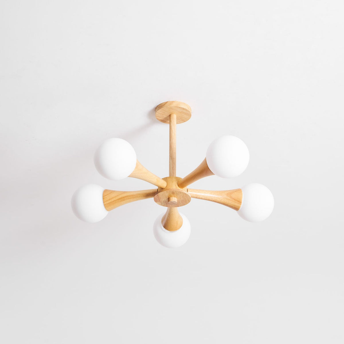 Side-angled view on a plain white background, this Clérachic chandelier's pale wood arms and opal globes are shown unlit.
