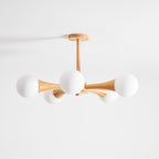 Rotated to a diagonal angle, this Clérachic chandelier's pale wood arms and opal glass globes sit unlit on a plain white background.