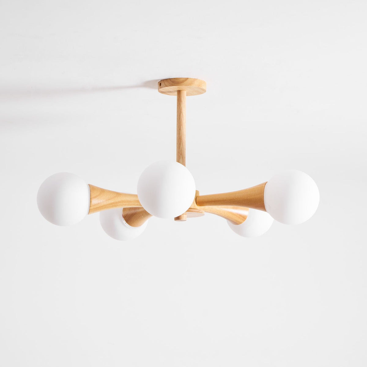 Rotated to a diagonal angle, this Clérachic chandelier's pale wood arms and opal glass globes sit unlit on a plain white background.