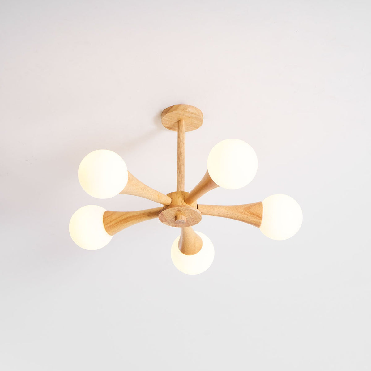 Shown at an angle on a plain grey background, this Clérachic chandelier's pale wood arms hold five unlit opal glass globes.