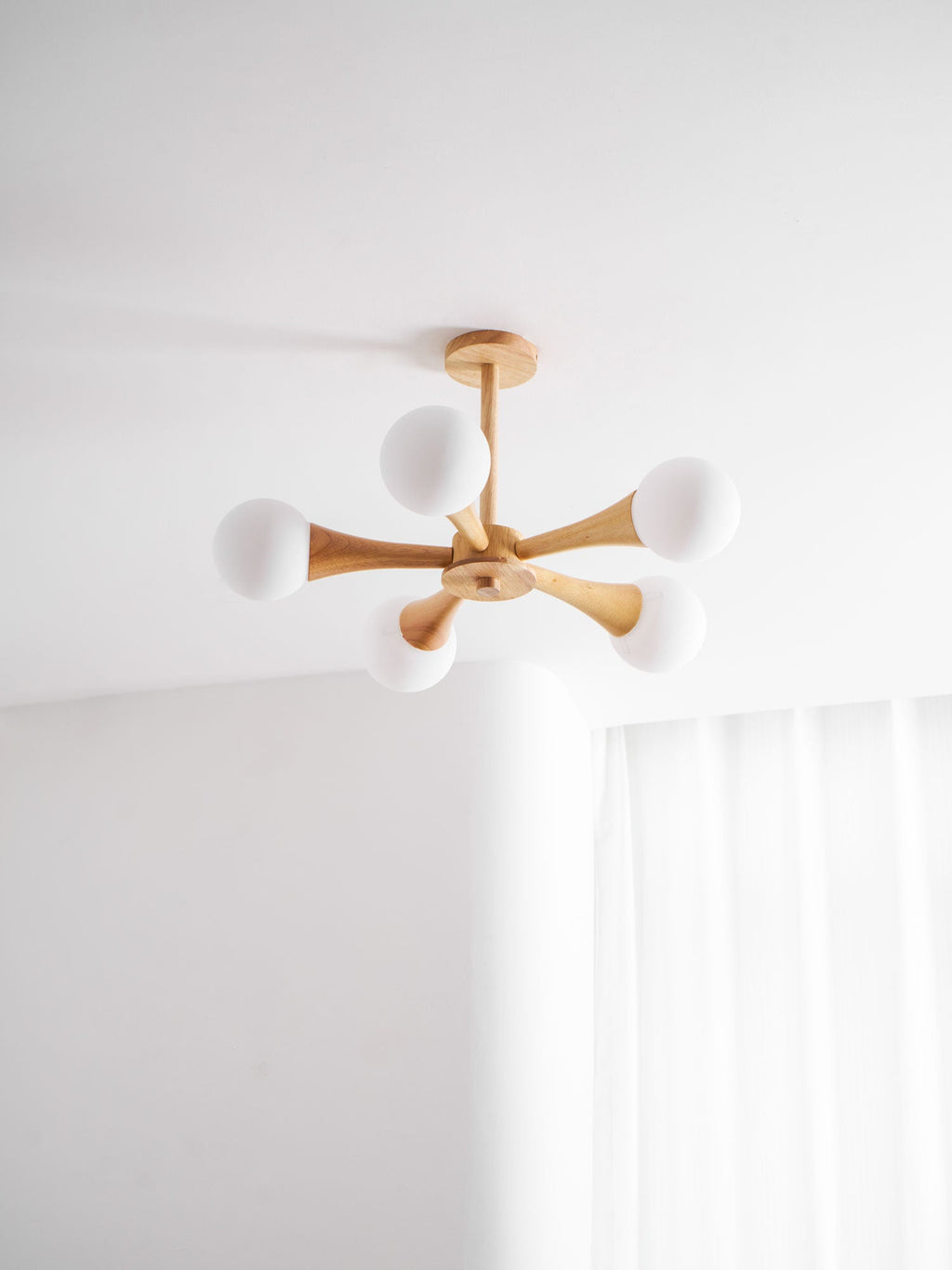 Seen close against a plain ceiling corner, this Clérachic chandelier's pale wood arms and glowing opal globes fan out from the centre hub.