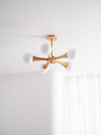 Seen close against a plain ceiling corner, this Clérachic chandelier's pale wood arms and glowing opal globes fan out from the centre hub.