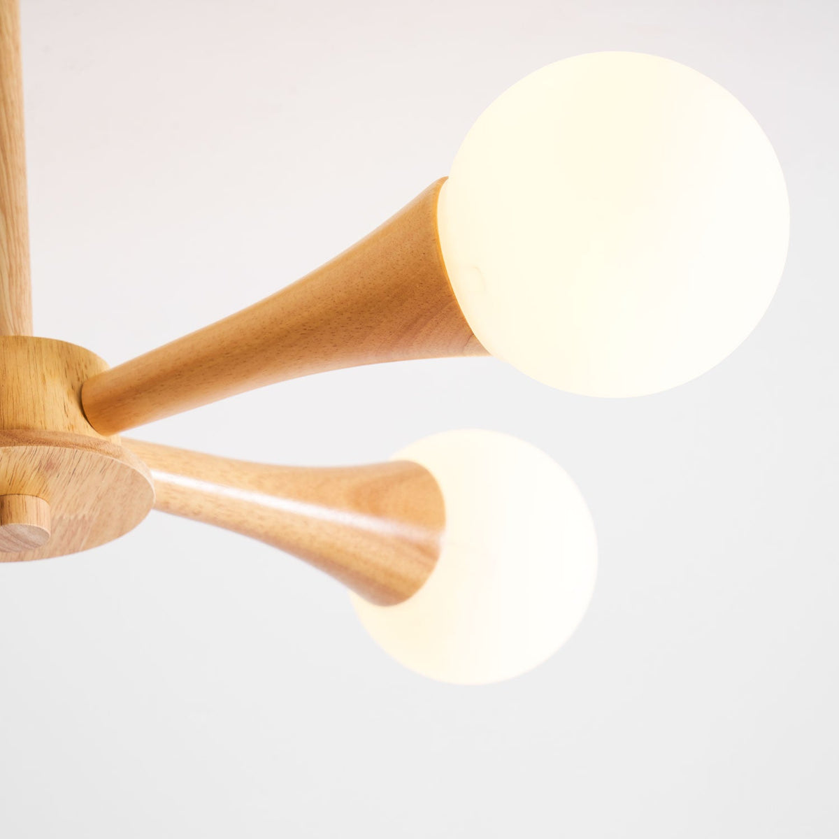 Close view of two opal glass globes glowing on their pale wood arms, showing the natural grain of this Clérachic chandelier.