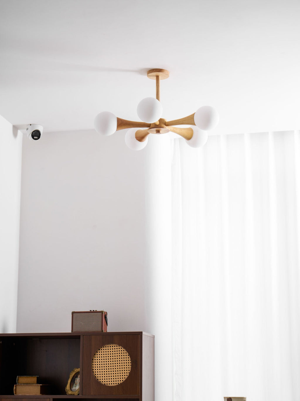 Mounted in a curtained corner with a small wall sensor nearby, this Clérachic chandelier glows above the dark wood cabinet below.