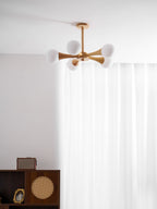 Glowing in a curtained room corner above a dark wood cabinet, this Clérachic chandelier's pale wood arms hold five lit opal globes.
