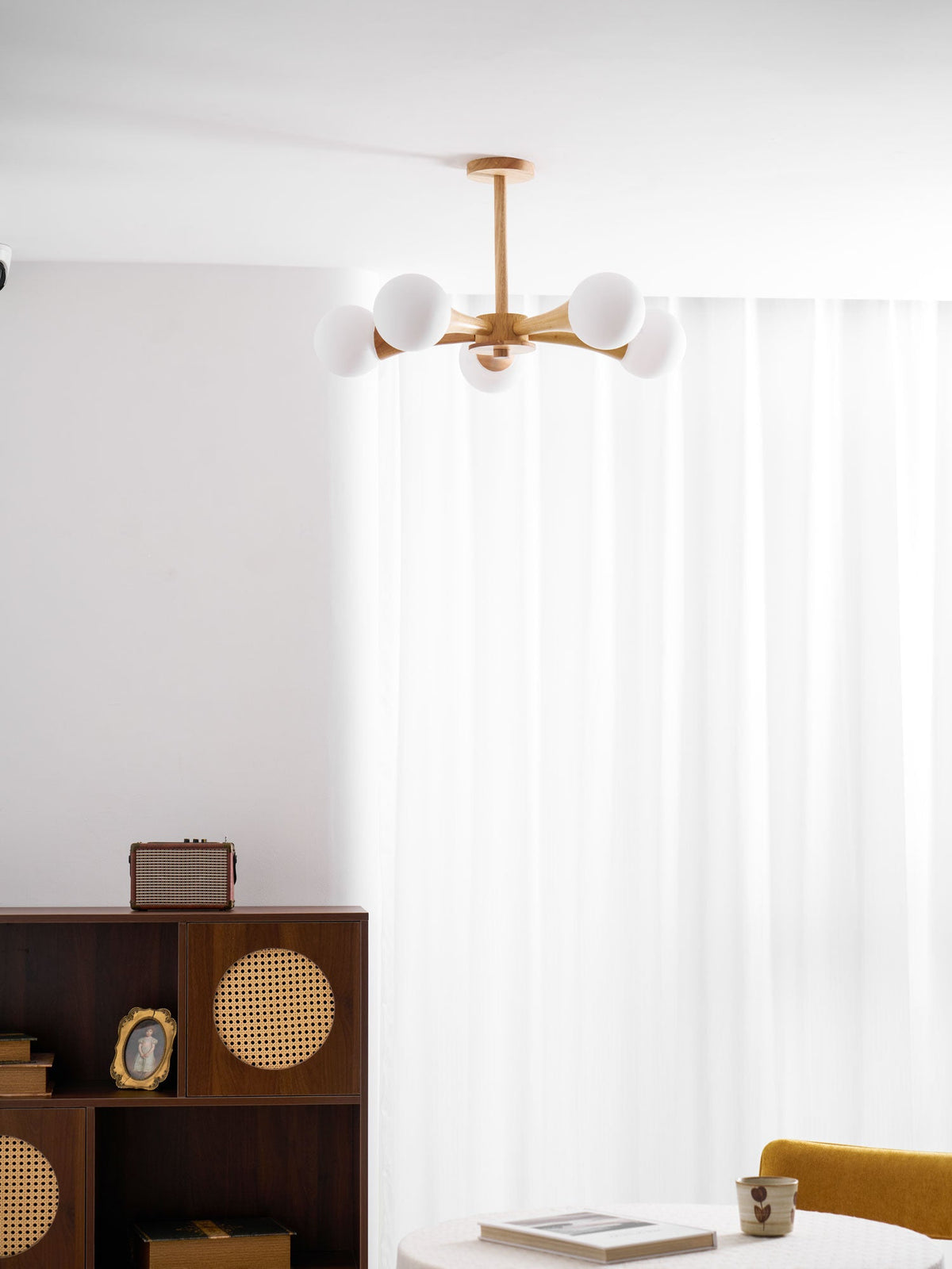 Wider view of a living corner with a record player and framed photo on a dark wood cabinet, this Clérachic chandelier glows above a mustard-yellow armchair.