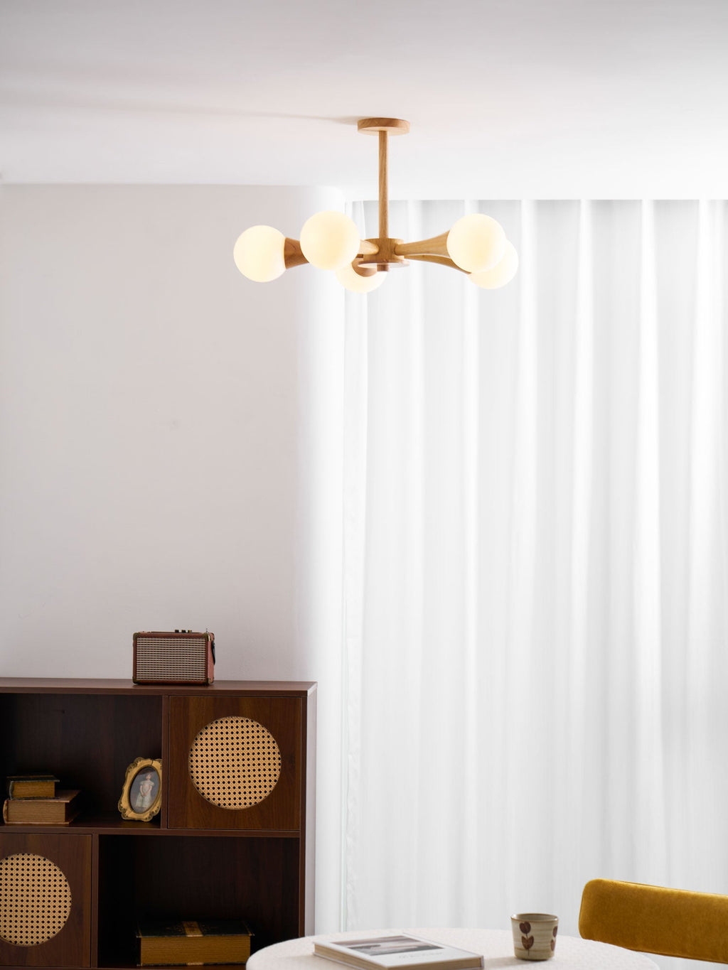 In a curtained room corner with a mustard-yellow chair and a record player on a dark wood cabinet, this Clérachic chandelier glows warmly.