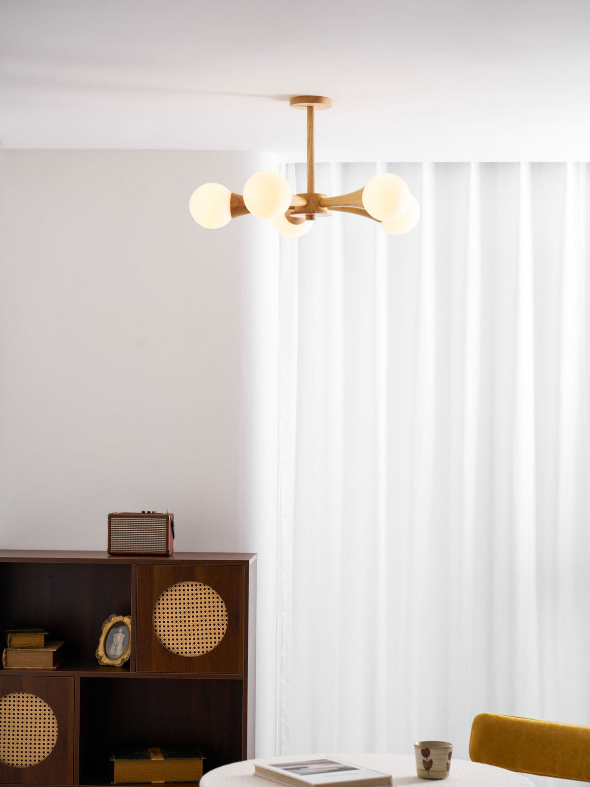 In a curtained room corner with a mustard-yellow chair and a record player on a dark wood cabinet, this Clérachic chandelier glows warmly.