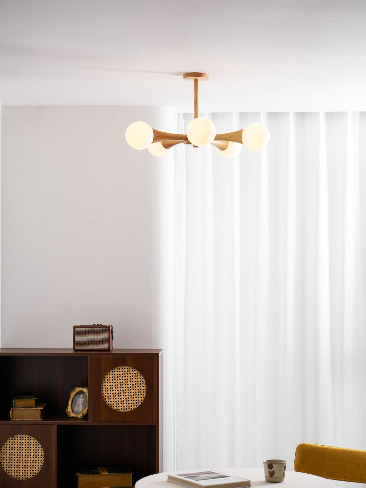 Cropped closer in the same curtained corner, this Clérachic chandelier's pale wood arms glow above the dark wood cabinet.