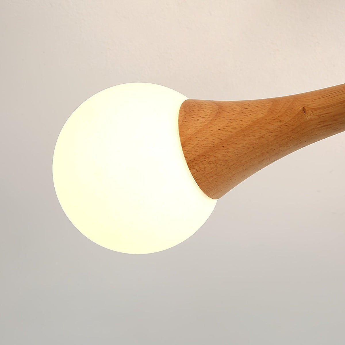 Close view of a single opal glass globe meeting a pale wood arm on this Clérachic chandelier, the grain visible beneath the warm glow.