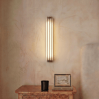 Clérachic marble and copper wall light seen straight on and lit, above a burl-wood chest with a black candle and a framed picture propped on a book.