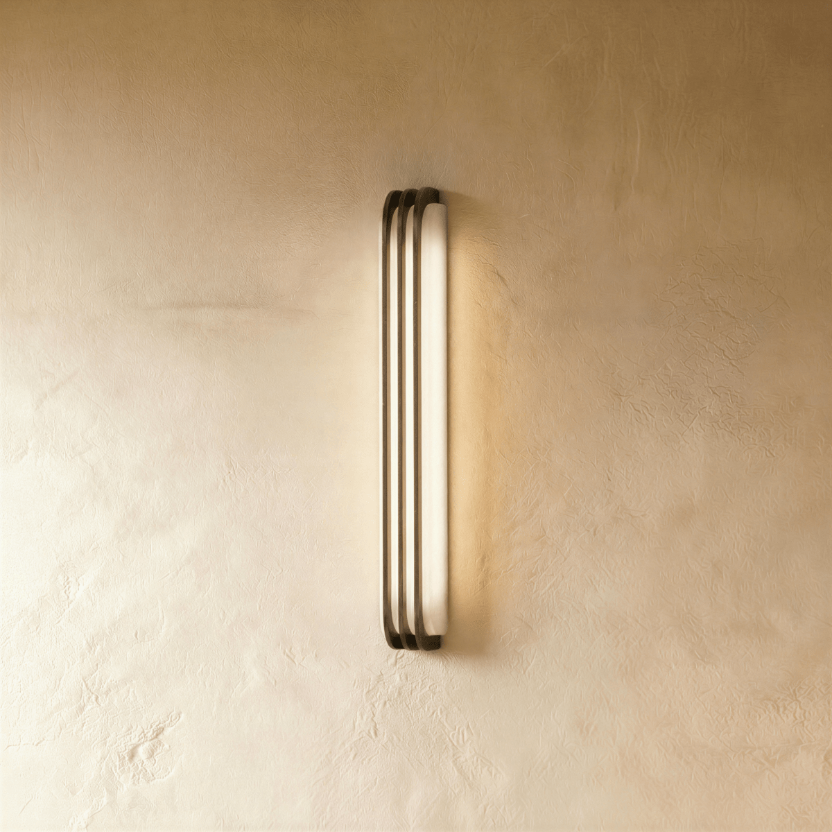 Clérachic marble and copper wall light seen at an angle, laying a soft halo of warm light across the plaster beside it.
