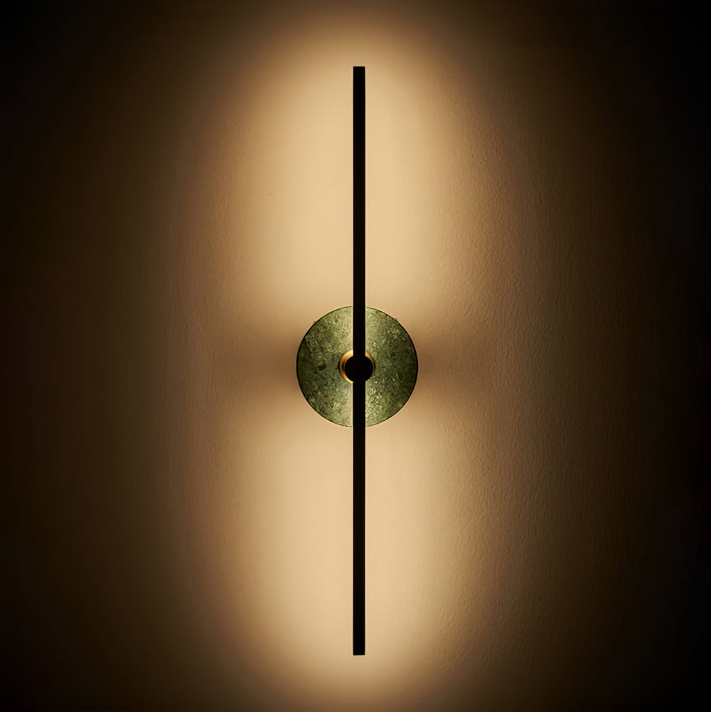 Clérachic wall sconce lit against a dark background, its green stone disc softly backlit by warm light.