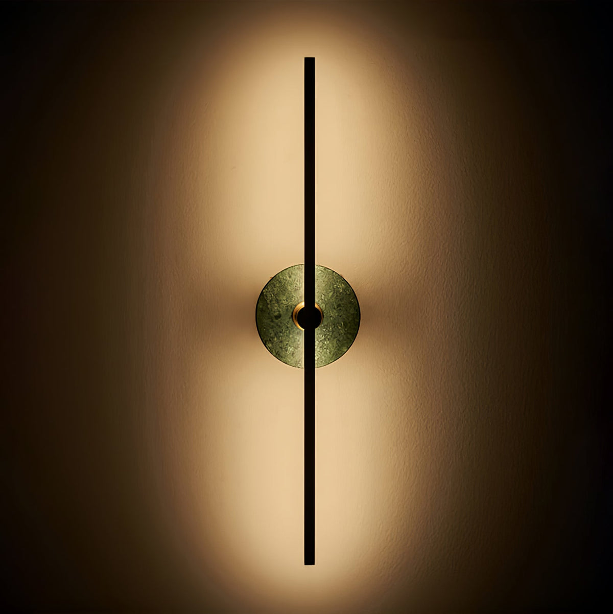 Clérachic wall sconce lit against a dark background, its green stone disc softly backlit by warm light.