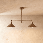 Clérachic chandelier in vintage brass, two angled cone shades hung from a slim rod against a plaster wall.