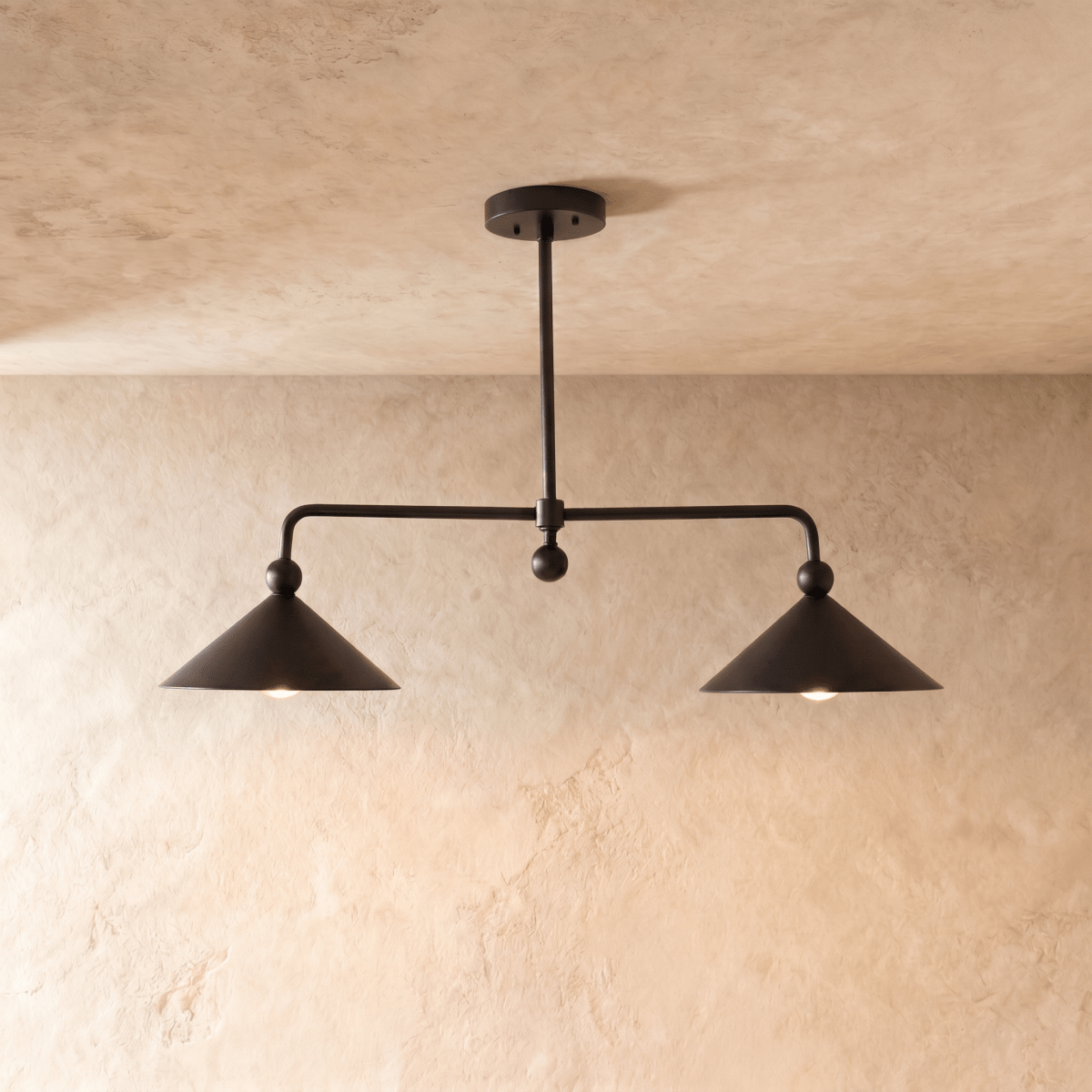 Clérachic chandelier in matte black, two cone shades hung from an angled ceiling bar over plaster.