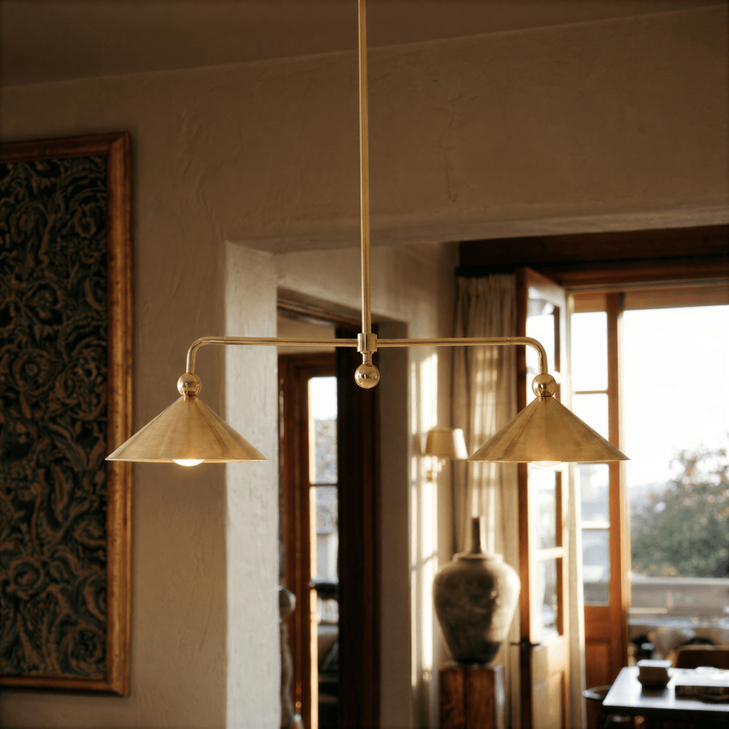 Clérachic chandelier in brass hanging over a sunlit living room with a tapestry, doorway and vase.
