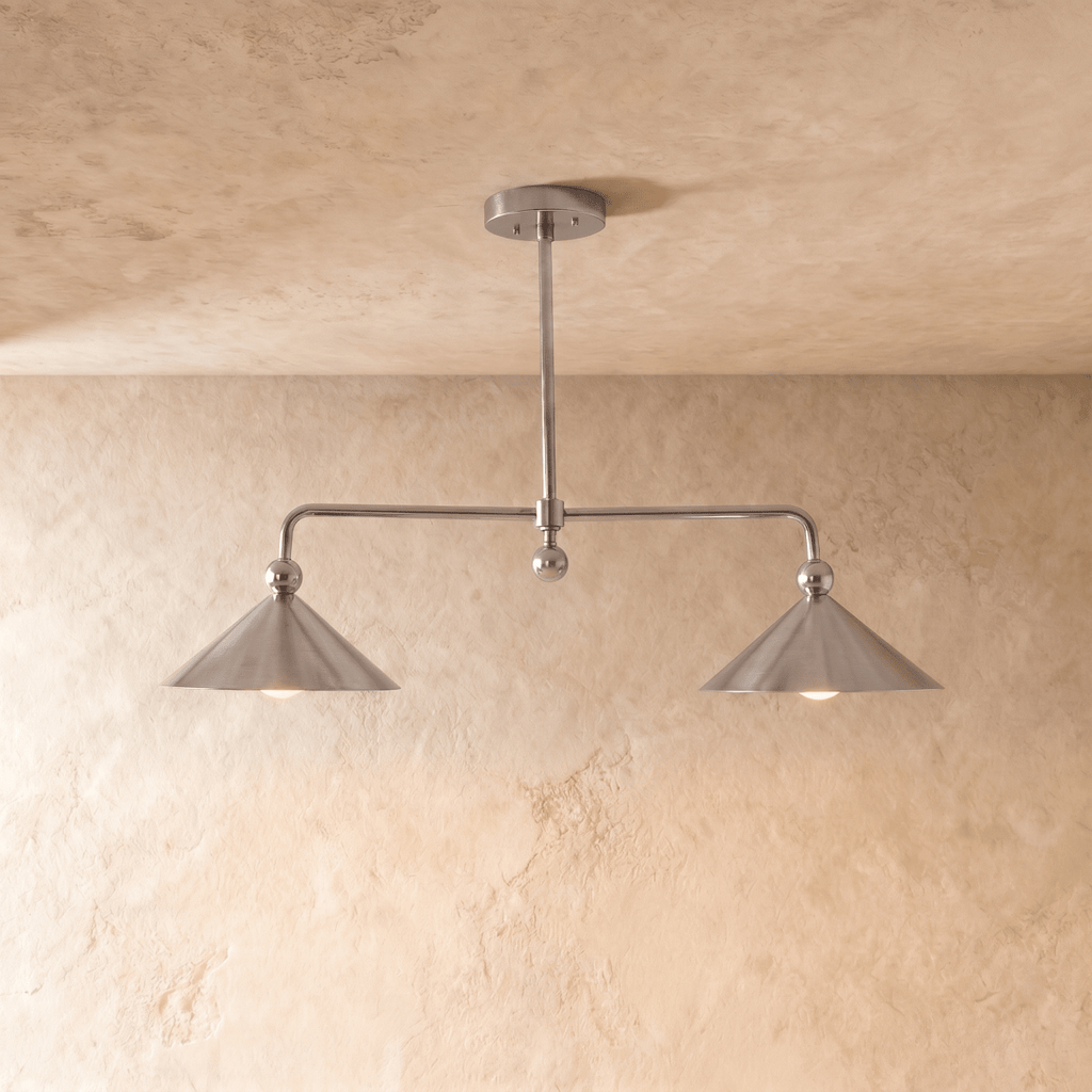 Clérachic chandelier in chrome, two cone shades on an angled bar set against a pale plaster wall.