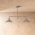Clérachic chandelier in chrome, two cone shades on an angled bar set against a pale plaster wall.