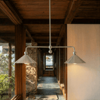 Clérachic chandelier in chrome hung in a timber-beamed corridor lined with a rough stone pillar.