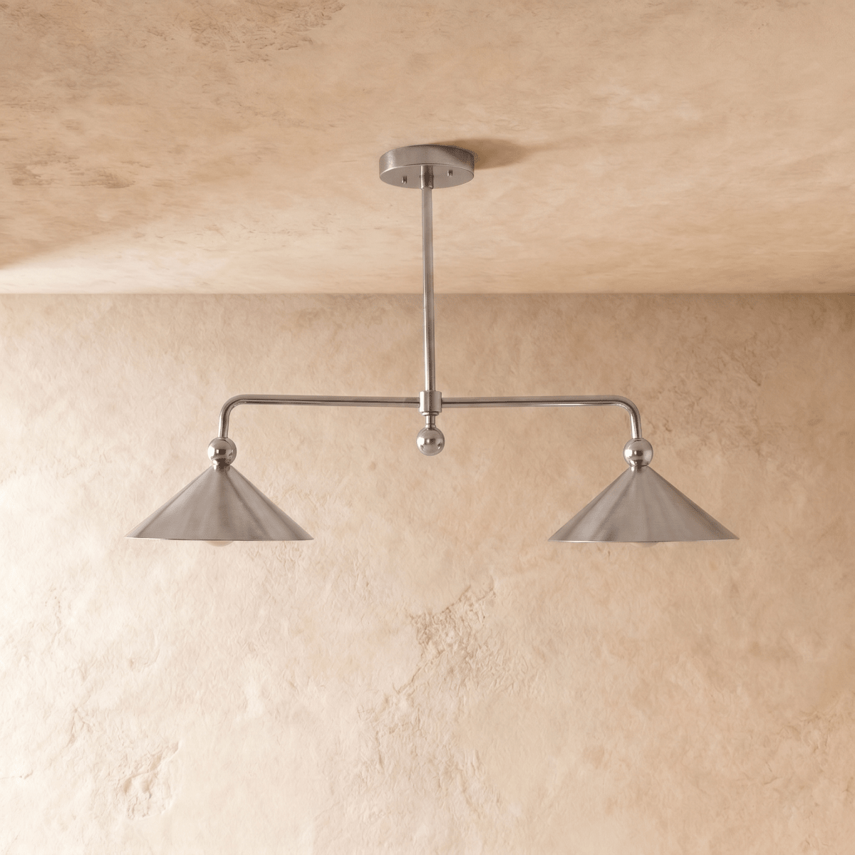 Clérachic chandelier in chrome, softly lit view of the paired cone shades and slender ceiling rod.