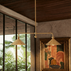 Clérachic chandelier in brass hanging beside a framed painting and a window looking onto greenery.