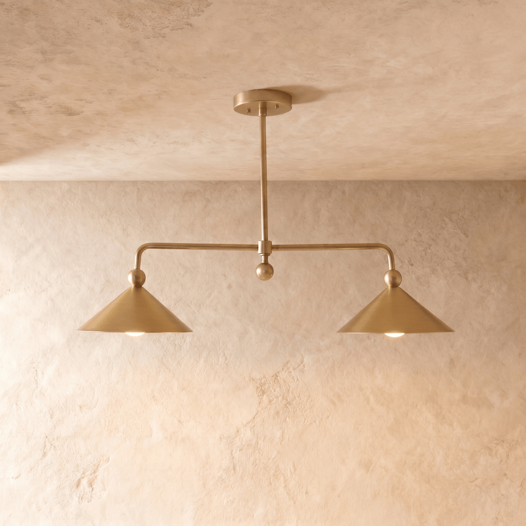 Clérachic chandelier in a warm satin brass finish, twin cone shades suspended from a slender ceiling rod.